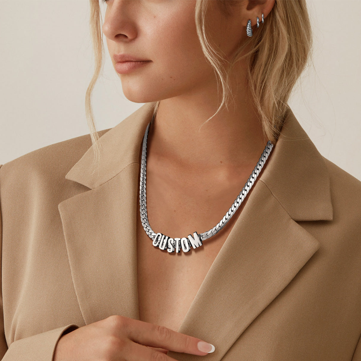 Person wearing a silver necklace with 'CUSTOM' pendant against a neutral background