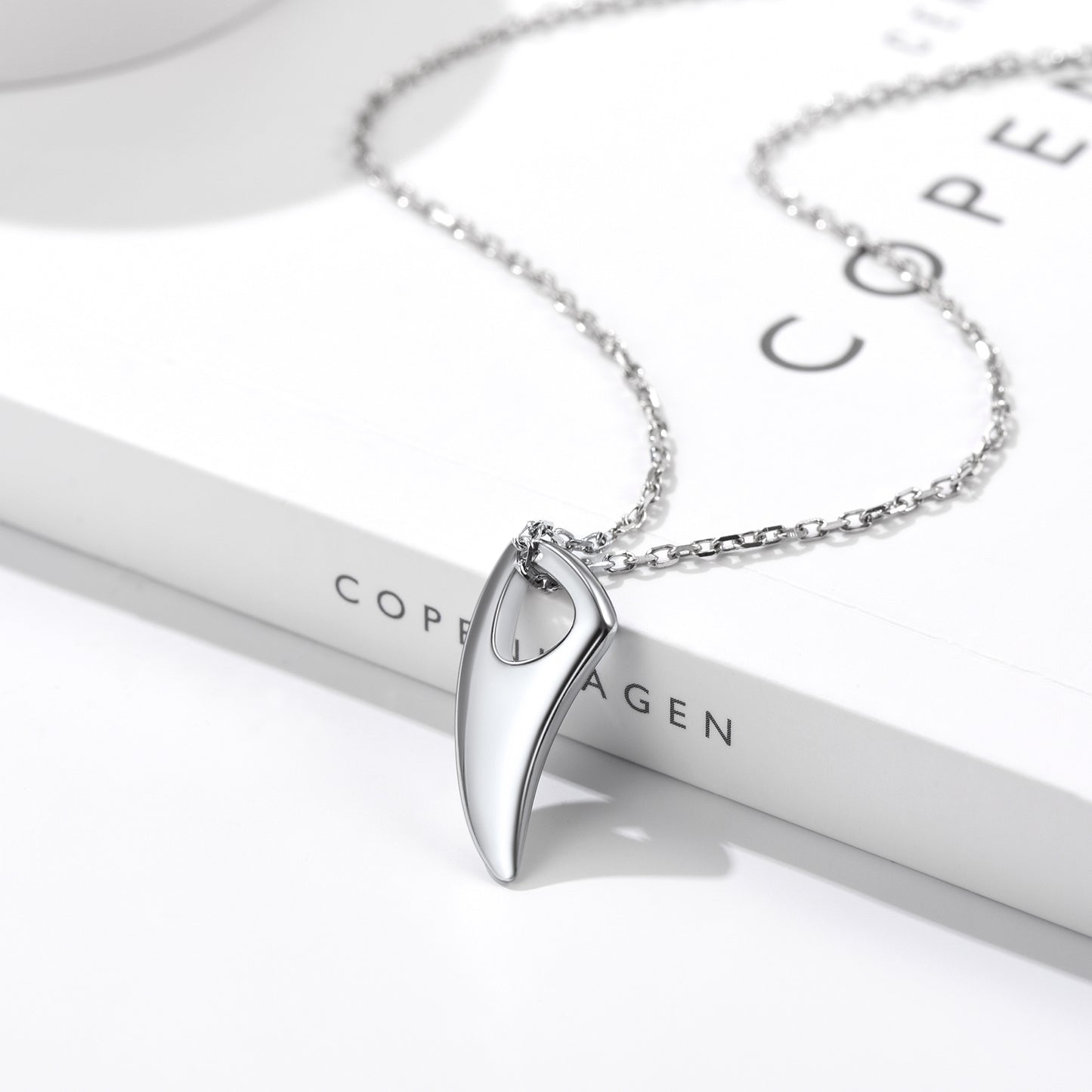 Silver necklace with a pendant on a white stand with 'Copenhagen' branding.