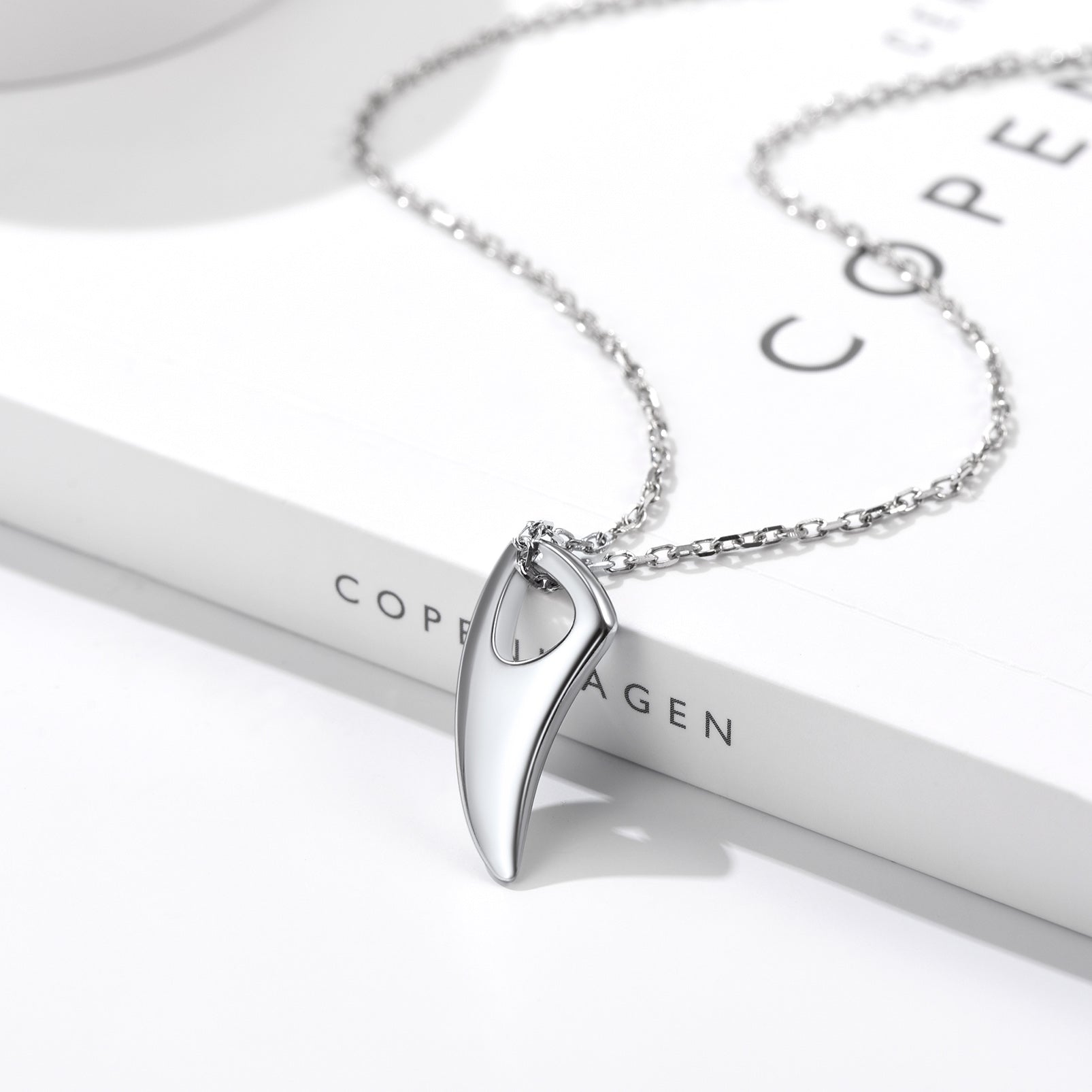 Silver necklace with a pendant on a white stand with 'Copenhagen' branding.