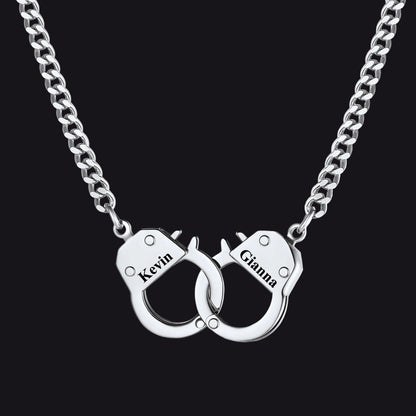 A silver chain necklace with a pendant shaped like two interlocking handcuffs. 