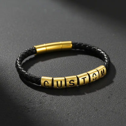 A black braided leather bracelet with a gold-plated cylindrical clasp and five gold letter beads spelling 'CUSTOM'.