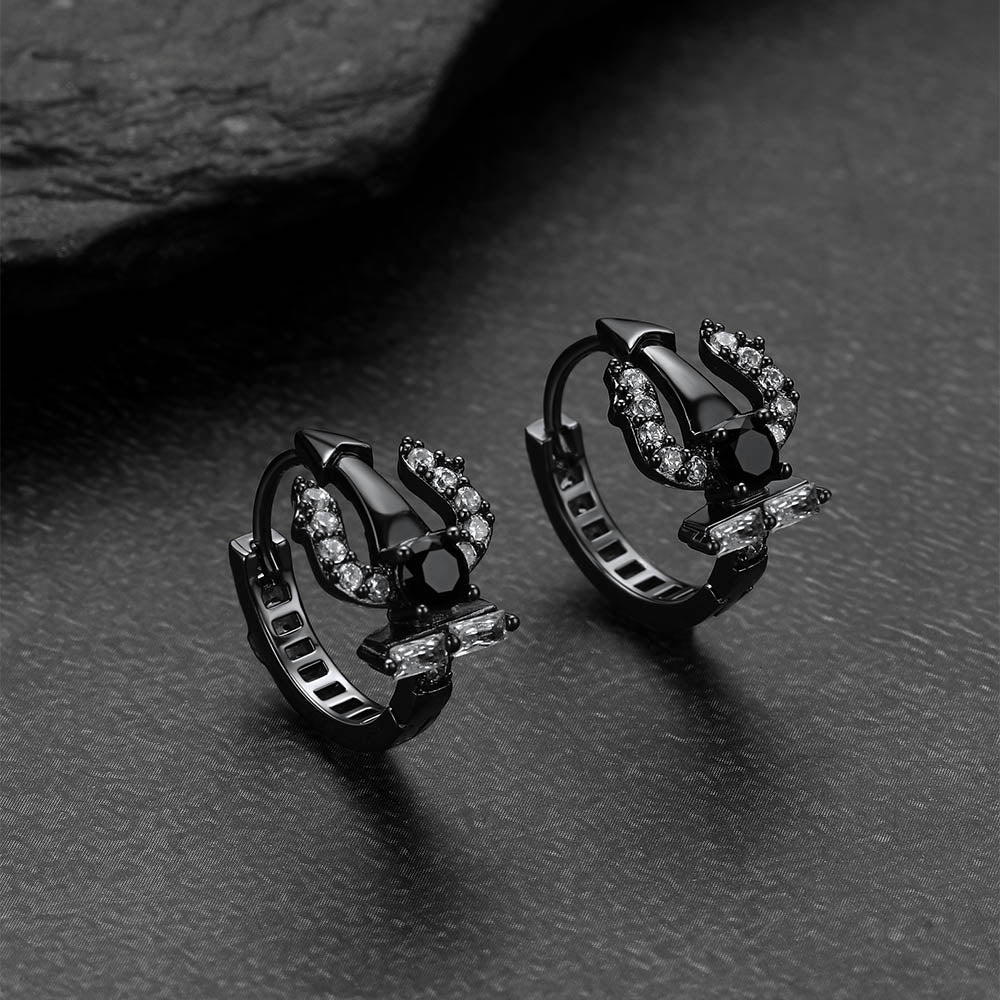 Pair of black Poseidon Trident Greek hoop earrings with gemstones on a dark surface