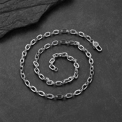 A silver-toned metal chain necklace with elongated oval links, arranged in a spiral on a dark textured slate surface.