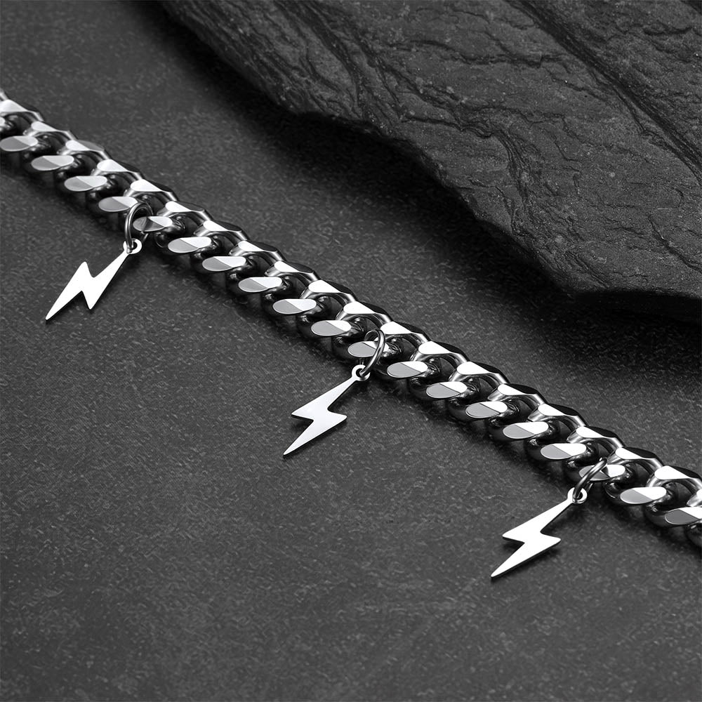 Silver chain with lightning bolt charms on a dark stone surface