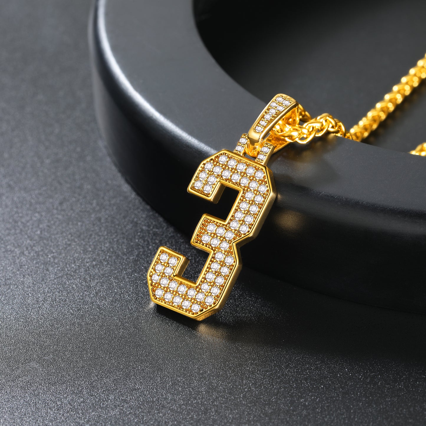 Gold necklace with a number '3' pendant on a black background