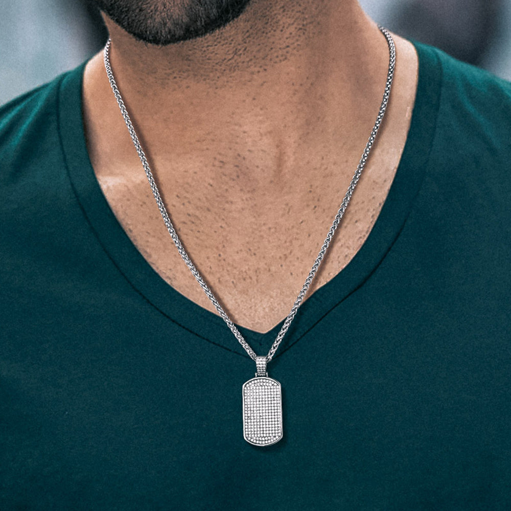Man wearing a silver necklace with a rectangular pendant on a blurred background