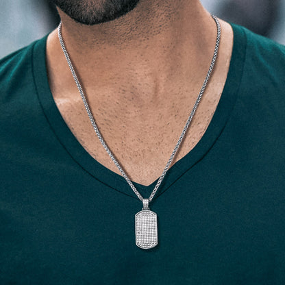 Man wearing a silver necklace with a rectangular pendant on a blurred background