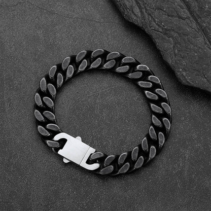 A black curb link chain bracelet, displayed on a dark textured slate surface.