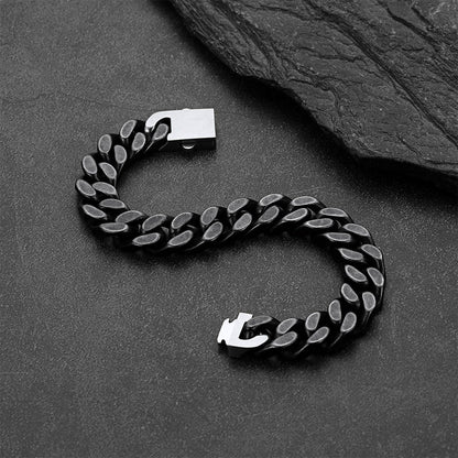 A black Cuban link chain bracelet, arranged in an S-shape on a dark textured surface with a slate prop.