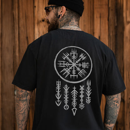 Man wearing a black t-shirt with a white viking symbol on the back, standing against a wooden wall.