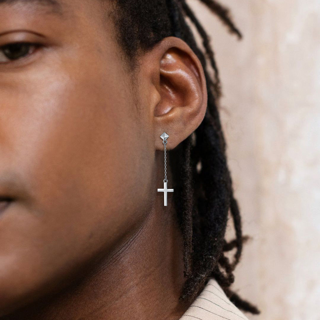 Close-up of a person wearing a silver cross earring with a blurred background