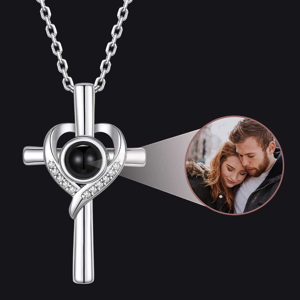 Silver cross necklace with heart design and black gemstone on a black background, inset with a couple photo.