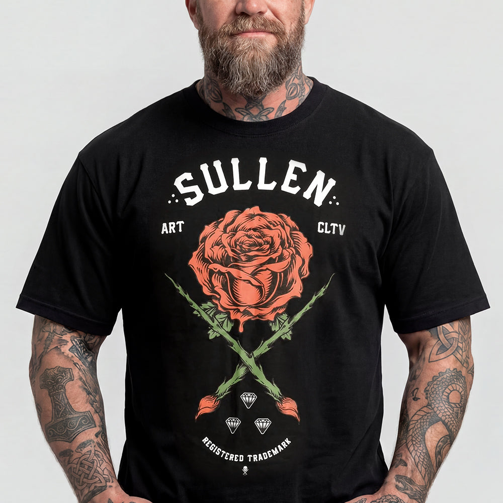 A man wearing a black graphic t-shirt with a large orange rose and white text reading 'SULLEN' on the front, set against a plain light gray background.