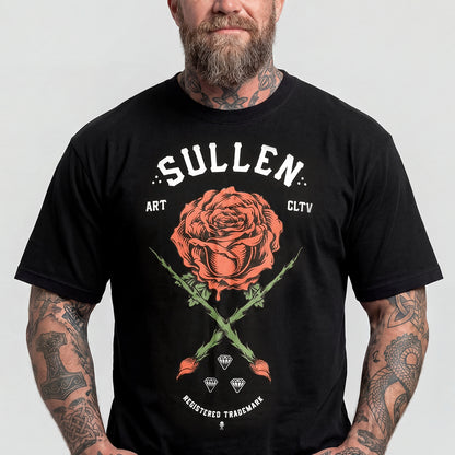 A man wearing a black graphic t-shirt with a large orange rose and white text reading 'SULLEN' on the front, set against a plain light gray background.