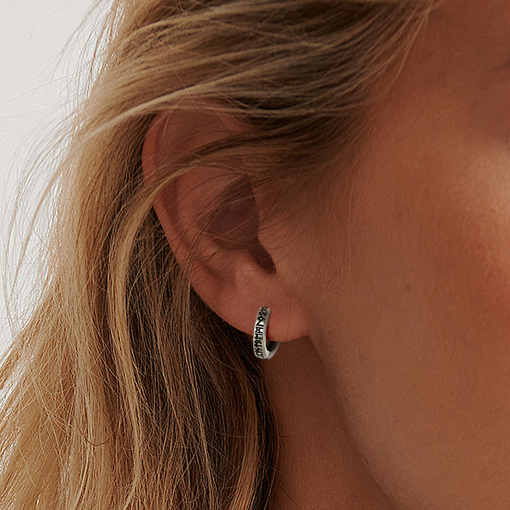 Close-up of an ear wearing a silver hoop earring with a blurred background