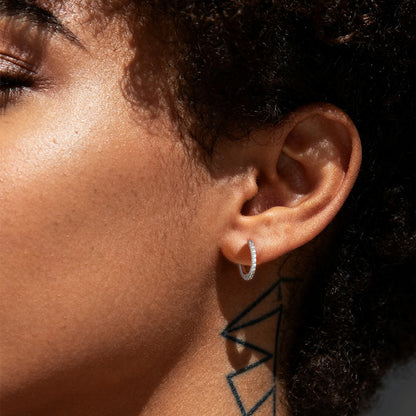 Close-up of a person wearing a silver hoop earring with a dark background