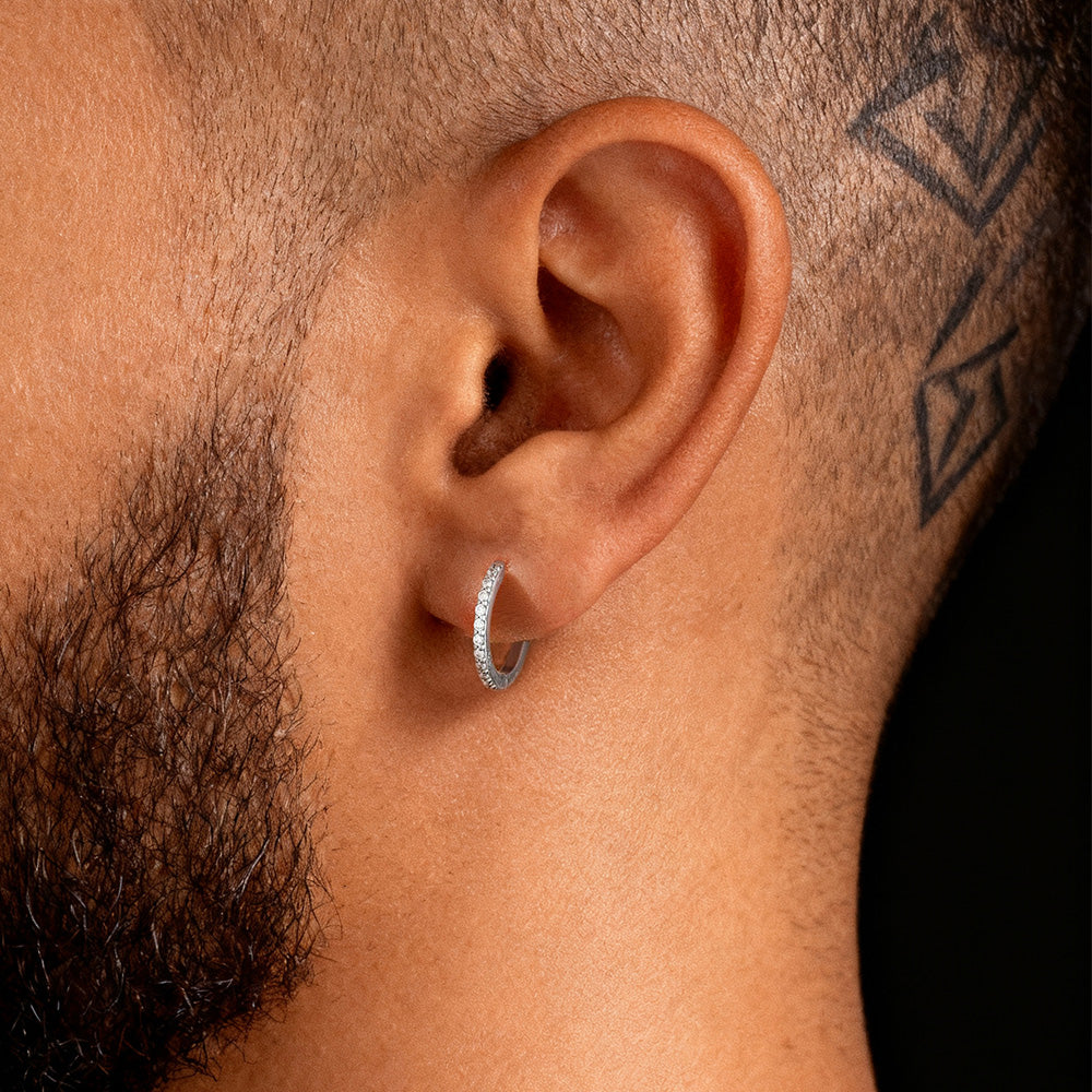 Close-up of an ear wearing a silver hoop earring with a tattoo on the neck.