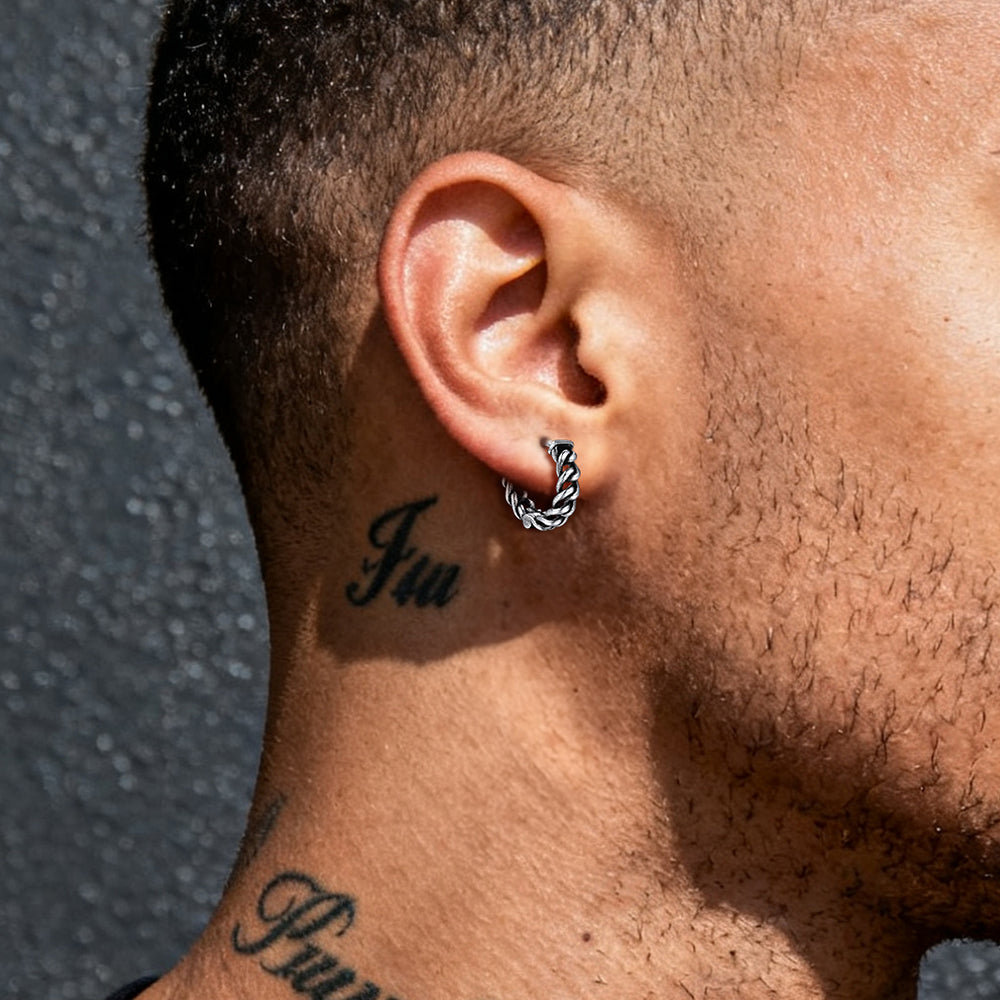 Close-up of a person's ear with a silver hoop earring and neck tattoos against a dark background.