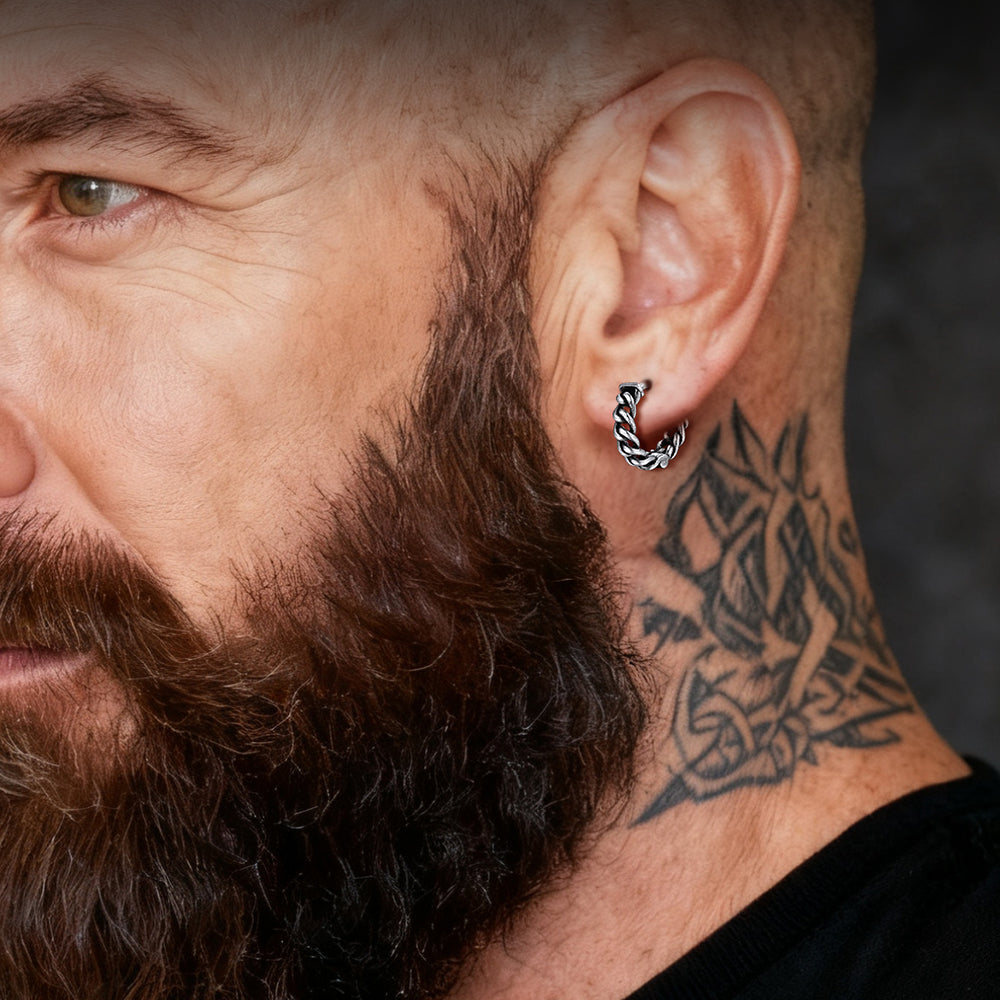 Close-up of a man with a beard, earring, and tattoo on his neck.