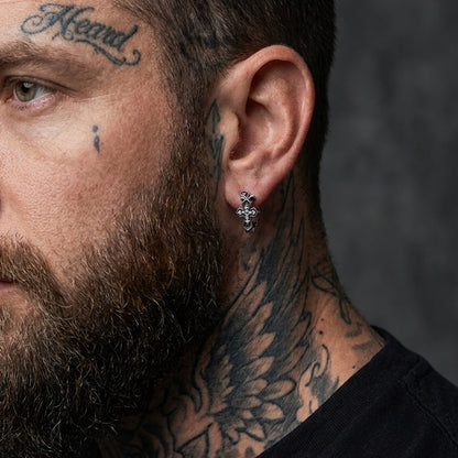 Close-up of a man with tattoos on his neck and face, wearing an CZ cross hoop earrings
