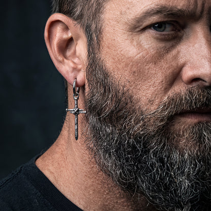 A close-up of a man's ear and side profile wearing a cross hoop earring against a dark background.