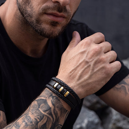 A close-up of a man's tattooed arm wearing a black leather bracelet