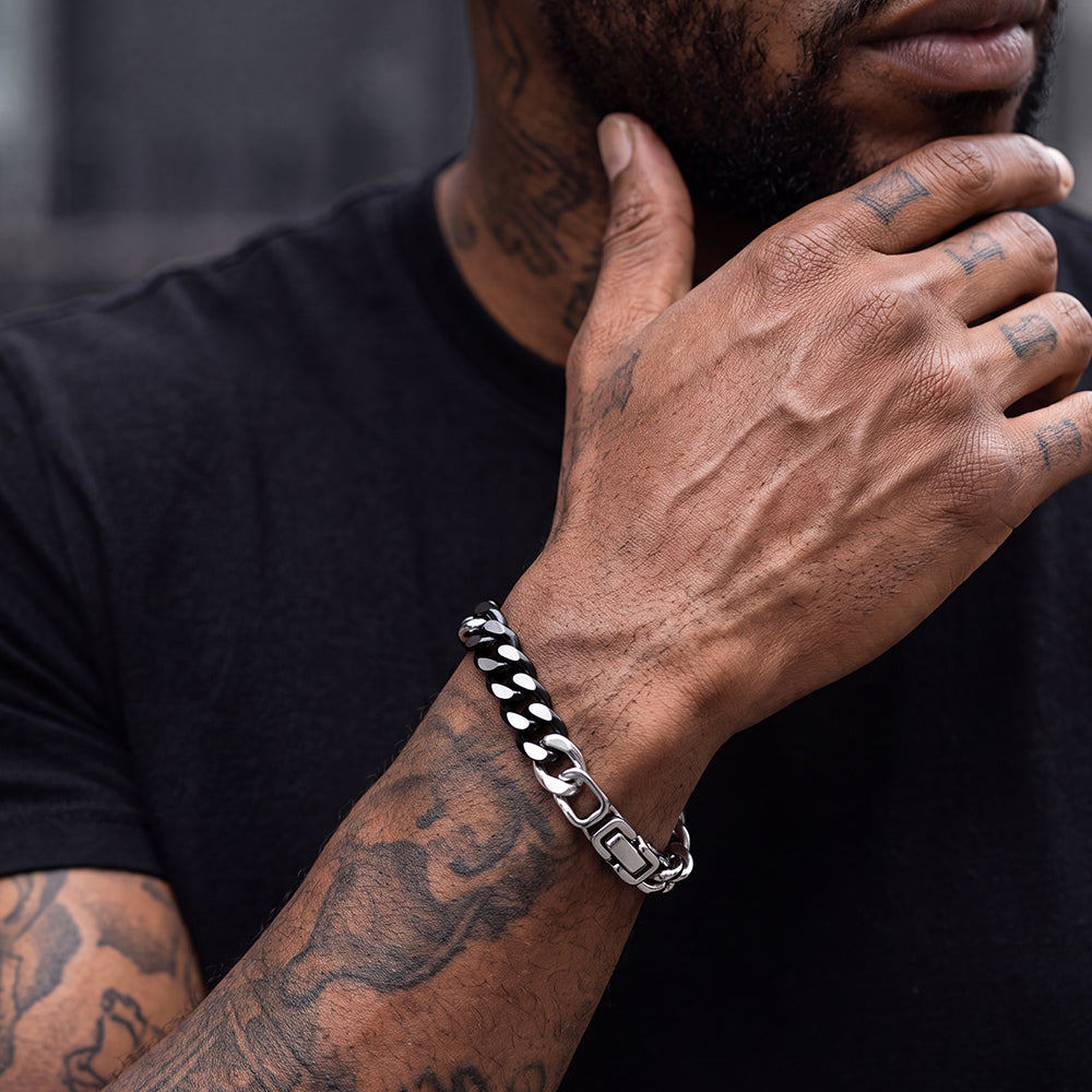 A close-up of a man's tattooed hand wearing a polished silver-toned curb chain bracelet.