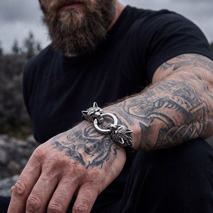 A close-up of a man's tattooed arm wearing a wolf-head leather bracelet.