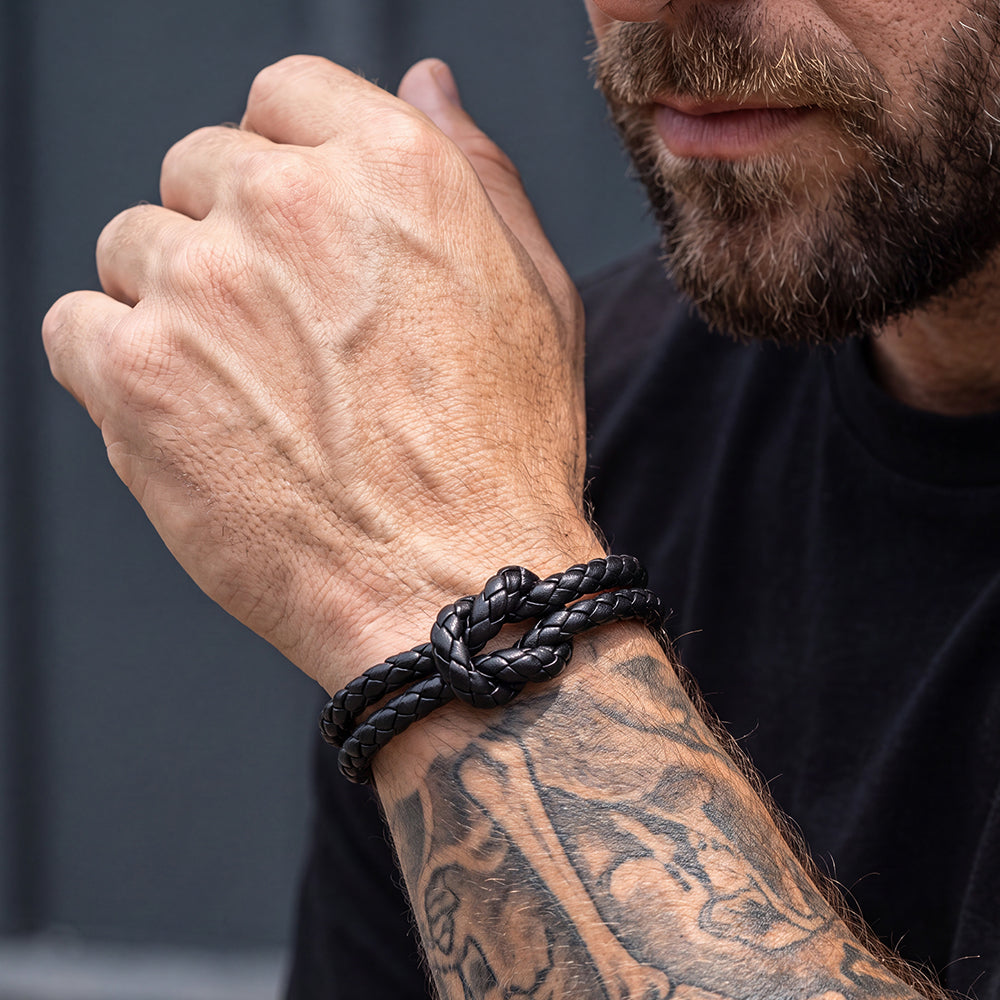 A close-up of a man's tattooed forearm wearing a black braided leather bracelet.