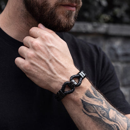 A close-up of a man's forearm and hand wearing a black braided leather chain-link bracelet.
