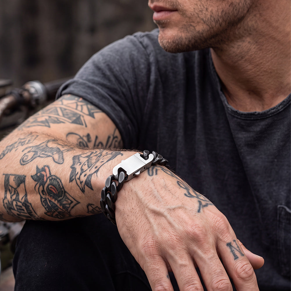 A close-up of a man's tattooed arm wearing a chain-link bracelet.