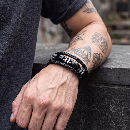 A close-up of a person's tattooed arm wearing black leather bracelets.