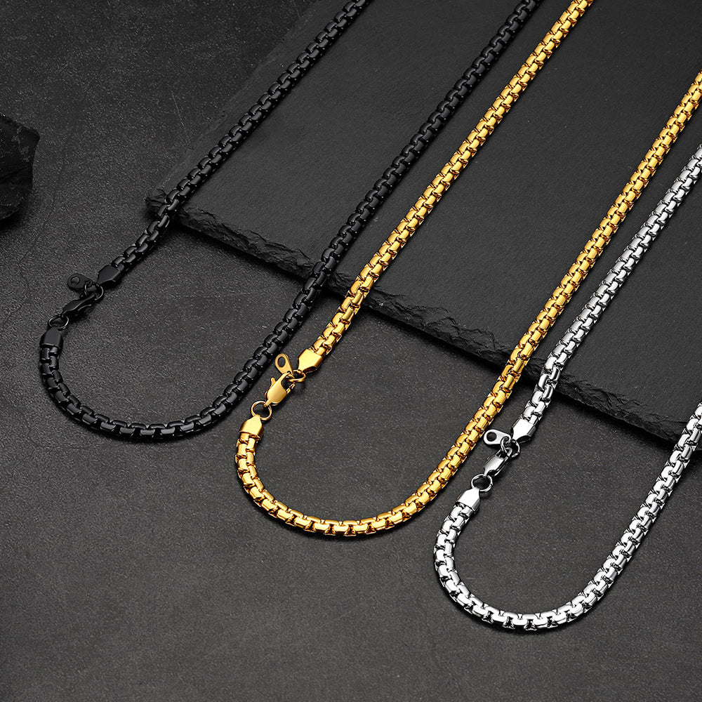 Three box chain necklaces in black, gold, and silver on a dark surface
