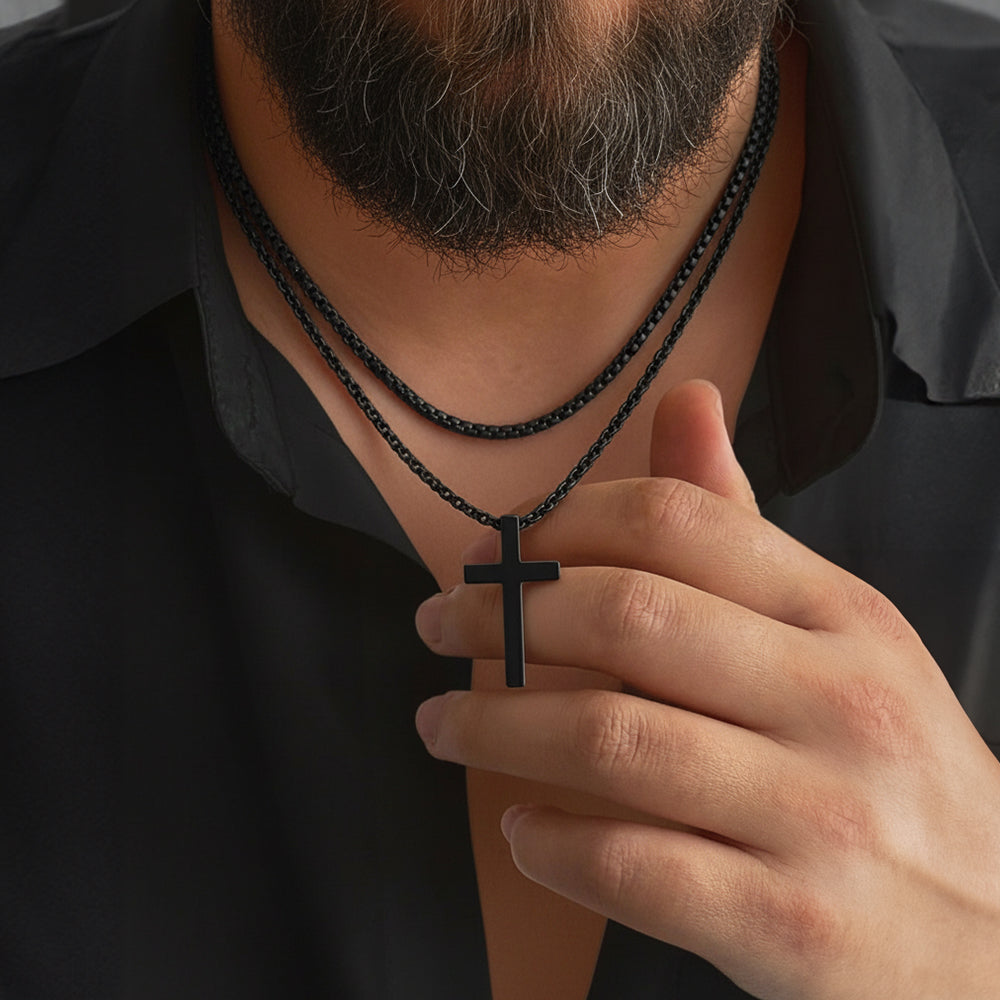 Person wearing a black cross necklace with a hand adjusting it against a dark background