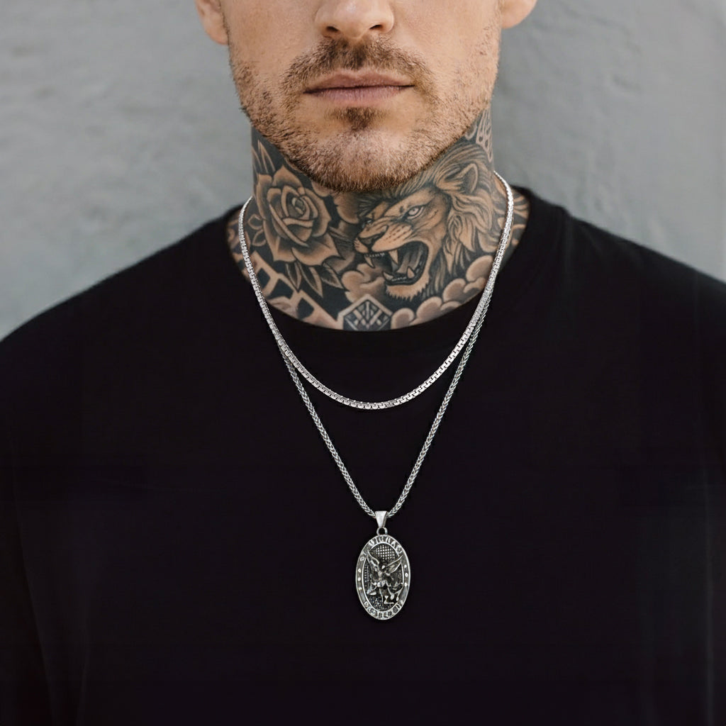 Man wearing a black turtleneck with a silver necklace featuring a lion pendant against a gray background