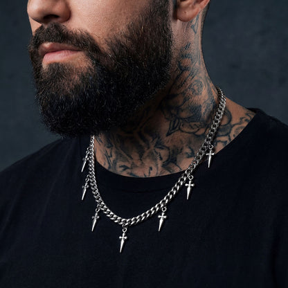 Man with tattoos wearing a chain necklace with spikes and crosses on a dark background