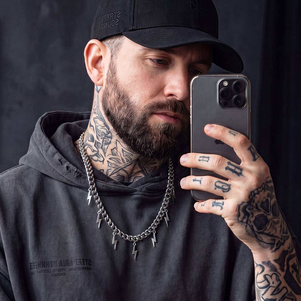 Man with tattoos taking a selfie with a phone against a dark background