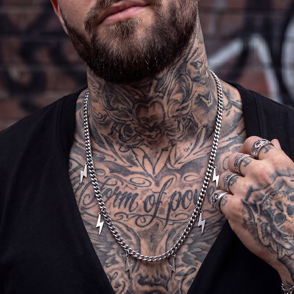 Man with tattoos on neck and arms wearing a silver chain necklace.