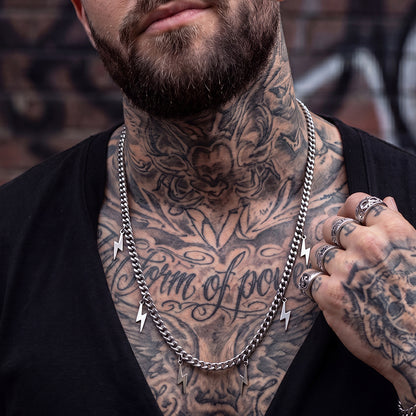 Man with tattoos on neck and arms wearing a silver chain necklace.