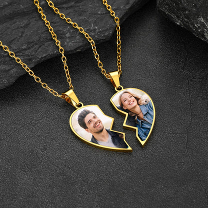 Gold necklace with a heart-shaped pendant featuring two people's photos on a dark stone surface.