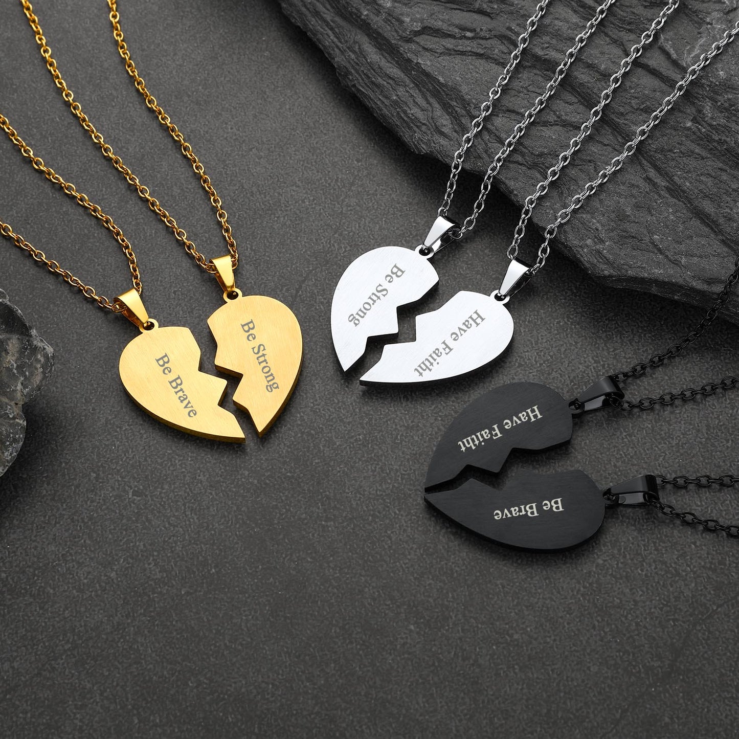 Three heart-shaped broken pendant necklaces in gold, silver, and black on a dark stone surface.