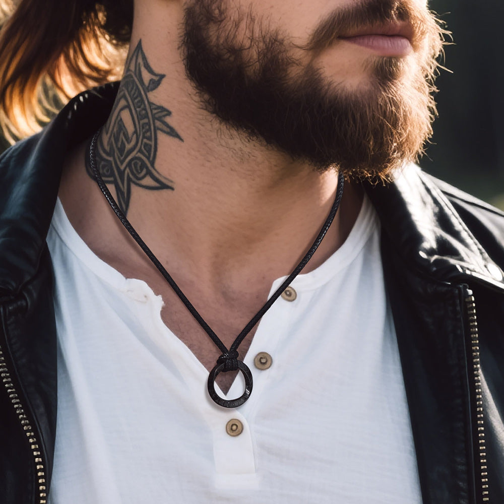 Man wearing a black leather necklace with a ring pendant, close-up of neck and tattoo.