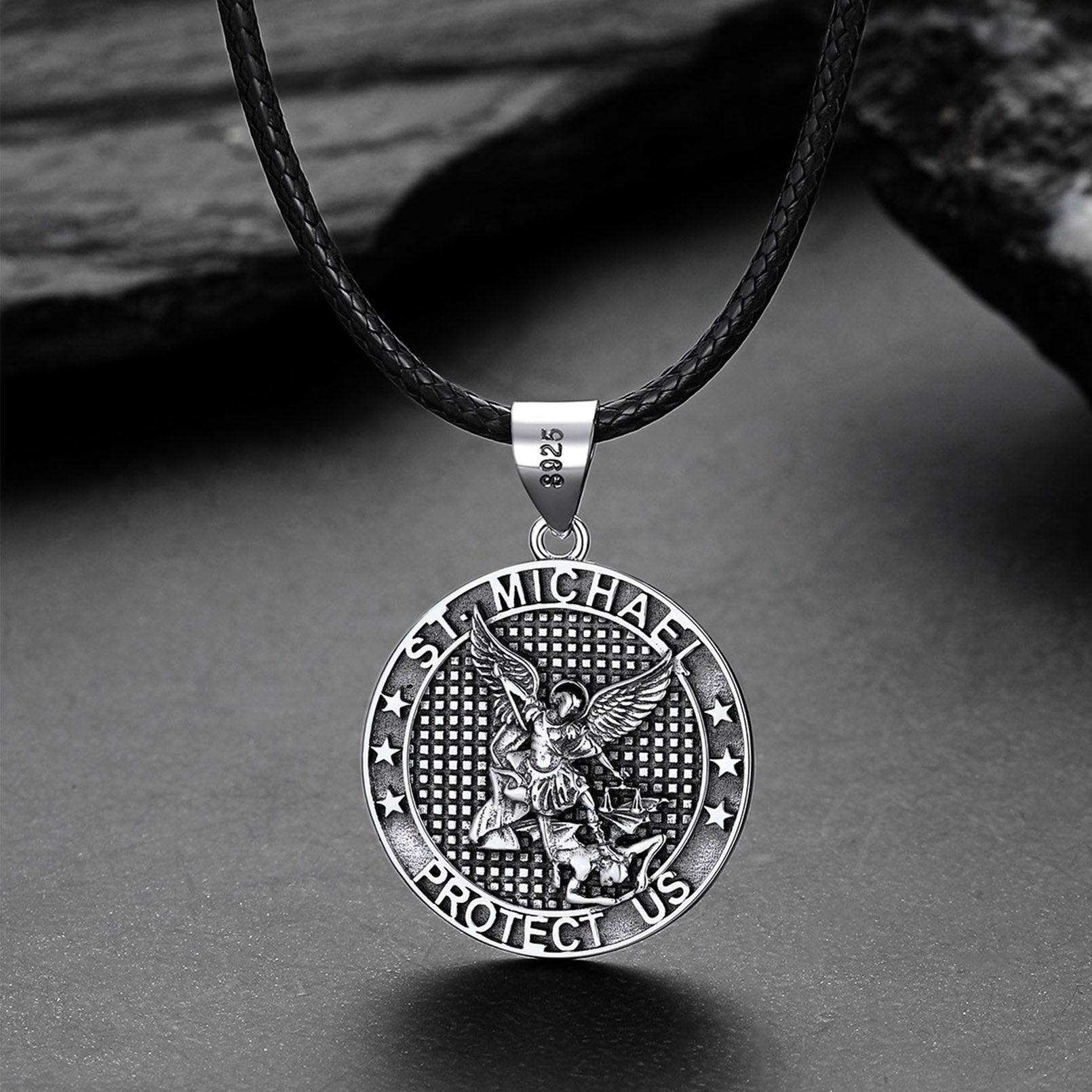 Silver Saint Michael pendant on a black leather cord against a gray background