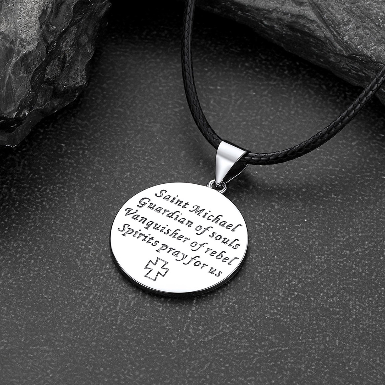 Round silver pendant with engraved text on a black cord against a dark stone background