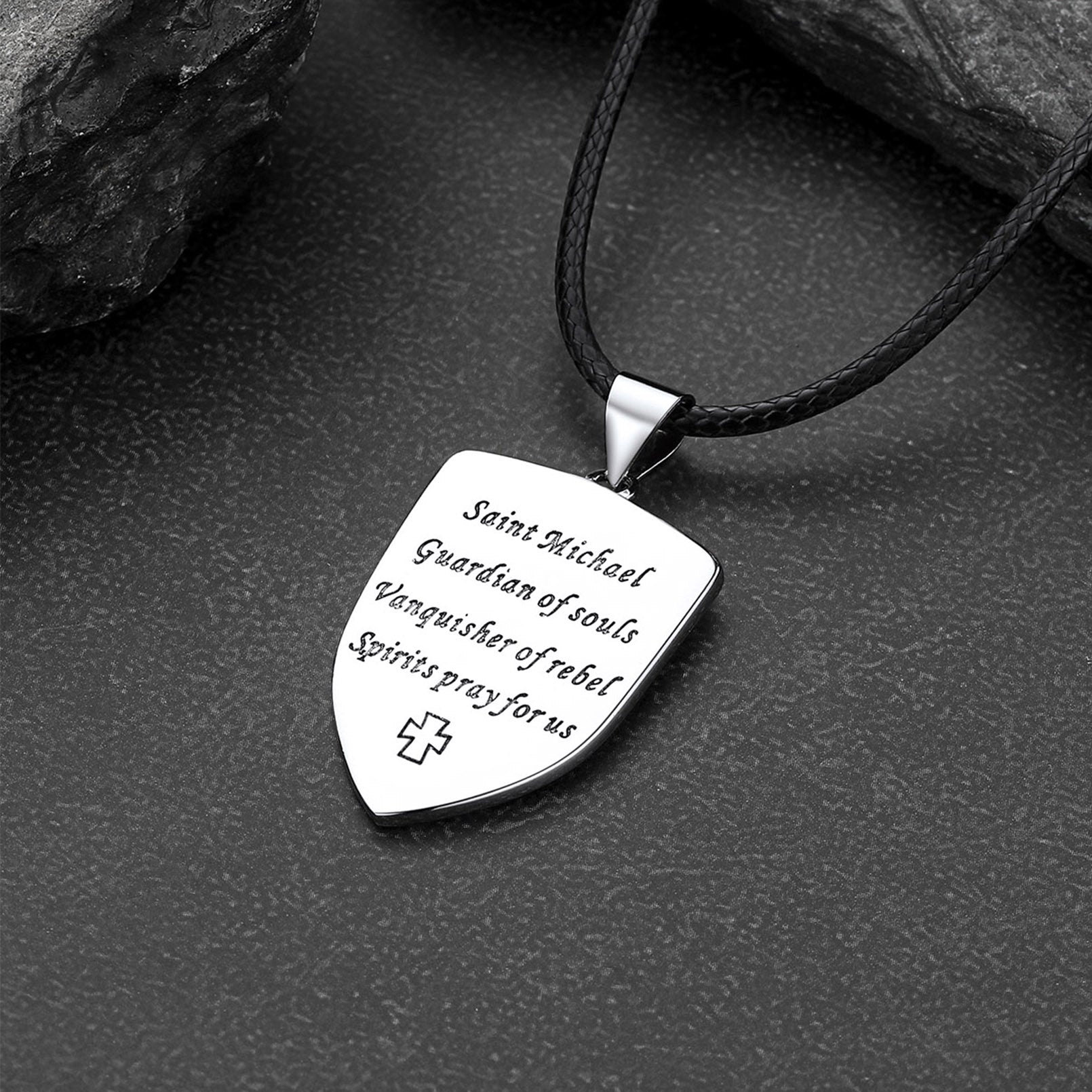 Silver pendant with engraved text on a black cord against a dark stone background