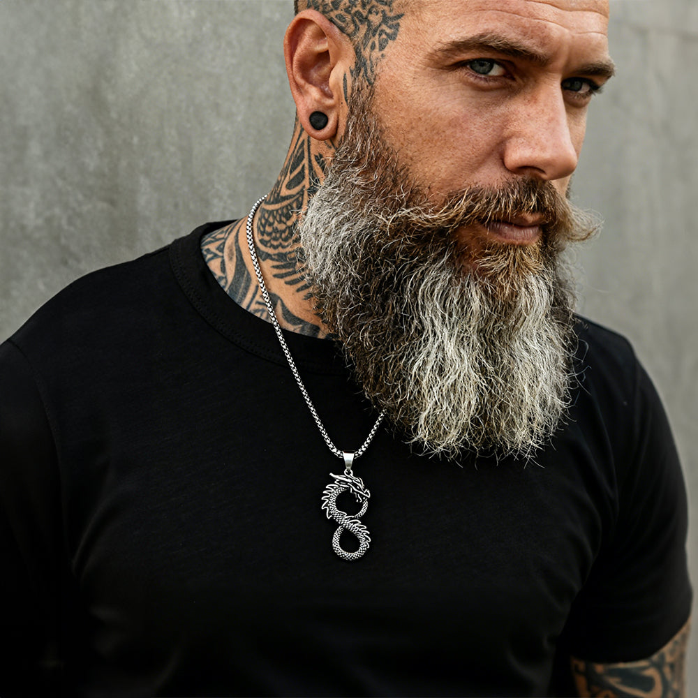 Man with tattoos and a beard wearing a black shirt and a silver necklace with a dragon pendant.