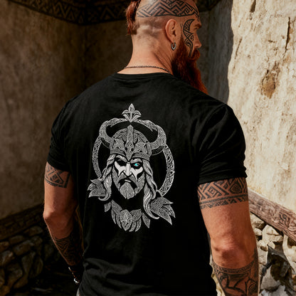 Man wearing a black t-shirt with a detailed viking design on the back, standing in a rustic setting.