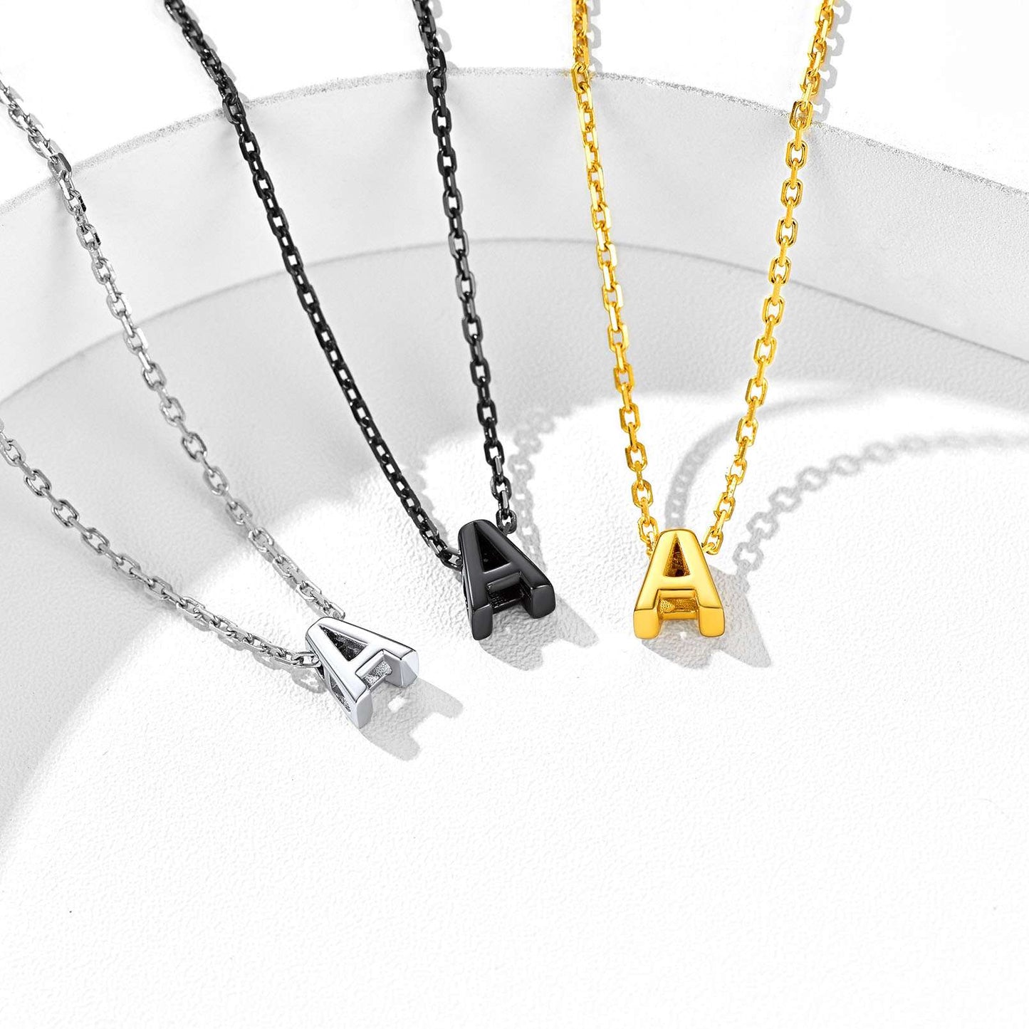 Three necklaces with 'A' initials in silver, black, gold