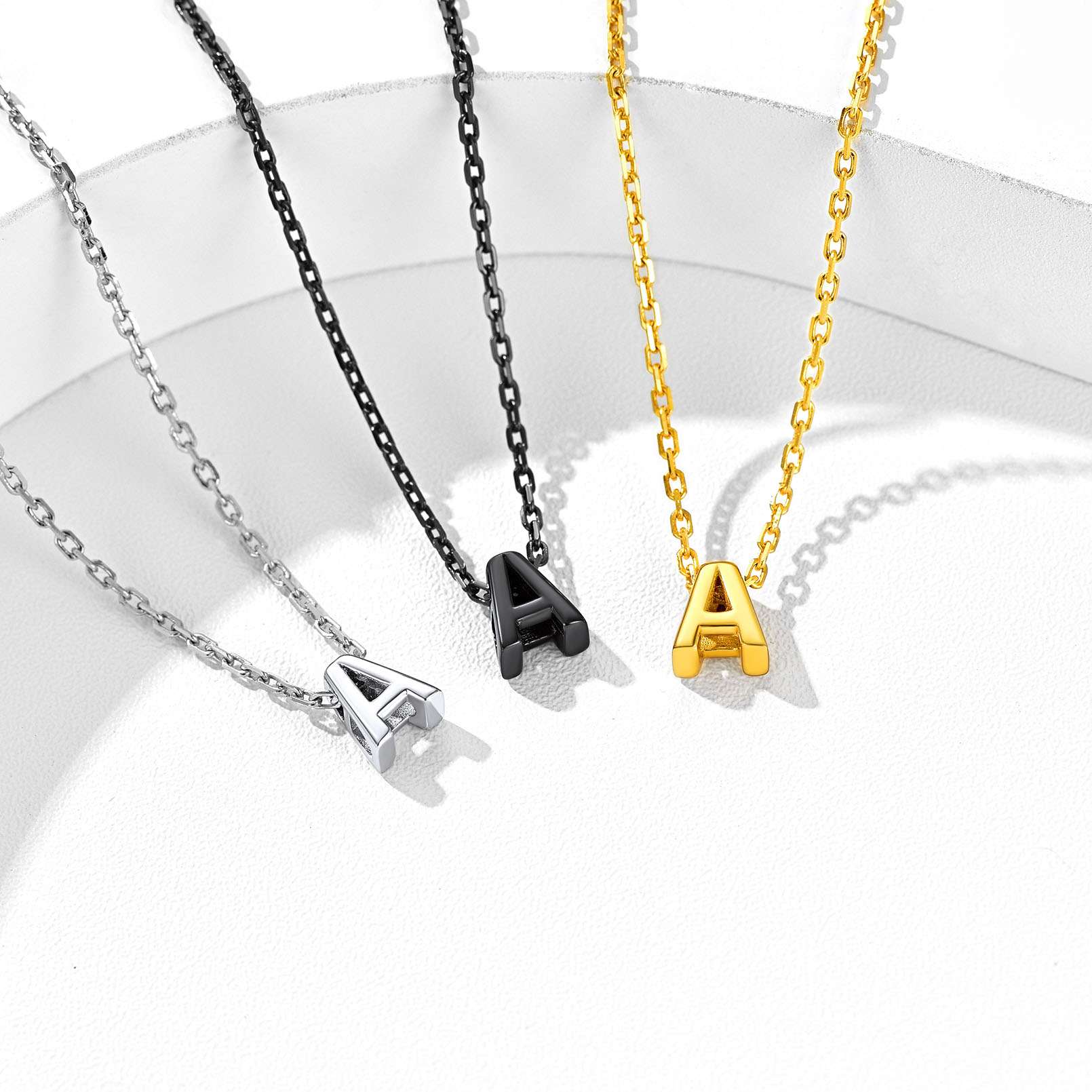 Three necklaces with 'A' initials in silver, black, gold