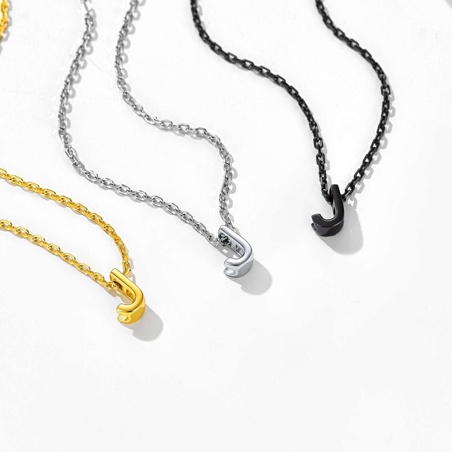 Three necklaces with 'J' initials in silver, black, gold
